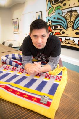 Louie Gong, owner of Eighth Generation, with one of the wool blankets he sells at his store in Pike Place Market. Photo by Wes Sauer