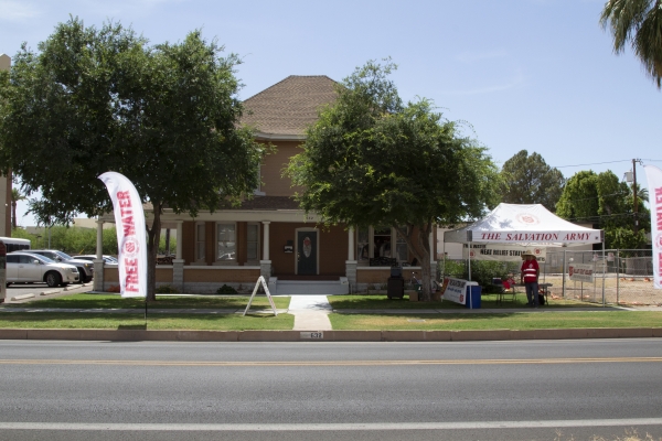 A large two-story mid-century residential-type house, seen from across the street, with two trees in front and a "Free Water" banner visible in yard as well as Salvation Army tent at side.