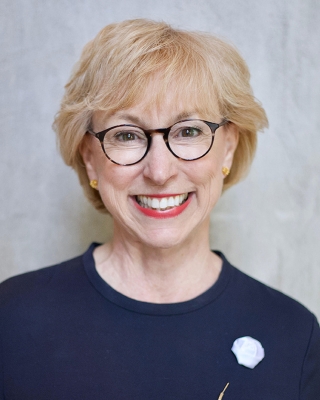 Smiling white woman in early middle age, seen from shoulders up, with short light-colored hair and round-framed glasses