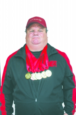 Middle-aged white man wearing red cap and six medals around neck