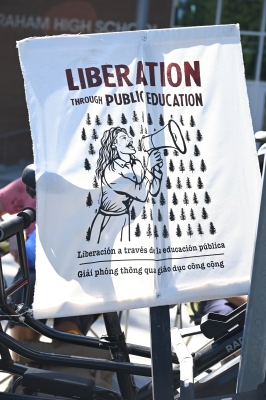 Banner showing drawing of woman speaking into megaphone, with text in English, Spanish, and Vietnamese reading, "Liberation through Public Education"