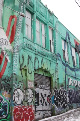 Side of blue-green painted building covered by different graffiti tags