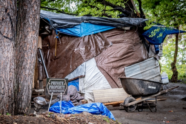 Tent made of brown and black sheets of tarp, strung between two trees, with manufactured sign outside it reading, "Private Property No Trespassing."