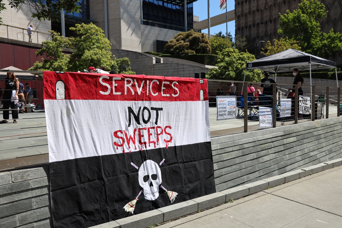 A red, black and white flag with a skull and crossed brooms and the slogan "Services Not Sweeps" on it.