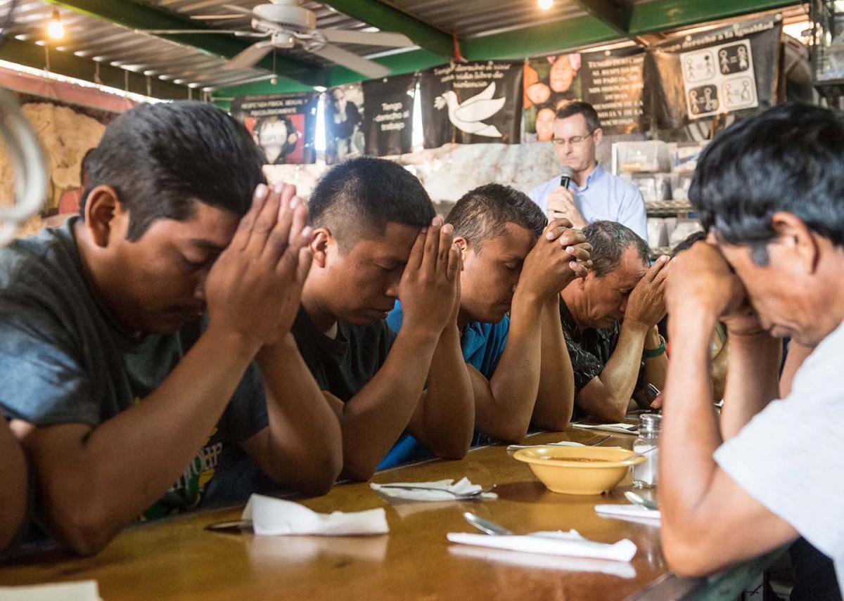 Migrants pray before a meal at El Comedor in Nogales, Mexico. Photo by Larry Hanelin.