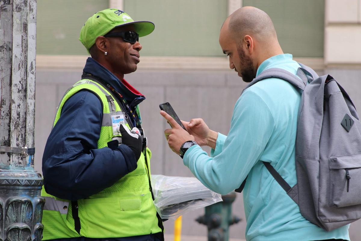 Zackary Tutwiler, left, sells a paper to Michael Charles who paid with Venmo. Offering simple, easy, smartphone payment is one way Real Change is helping vendors succeed. Photo by Jon Williams.