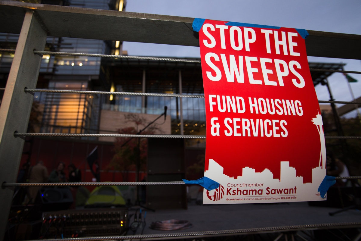 A sign reads "Stop the Sweeps: Fund Housing & Services"
