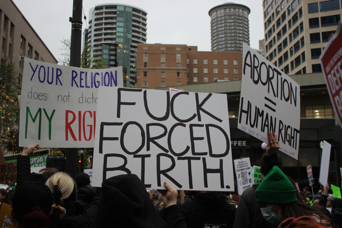 Close-up view of rally, with people holding signs; one in foreground reads, "Fuck Forced Birth."