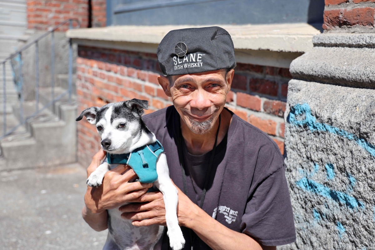 White man in gray cap, with gray goatee, holds a small black-and-white dog in his hands while smiling for the camera.