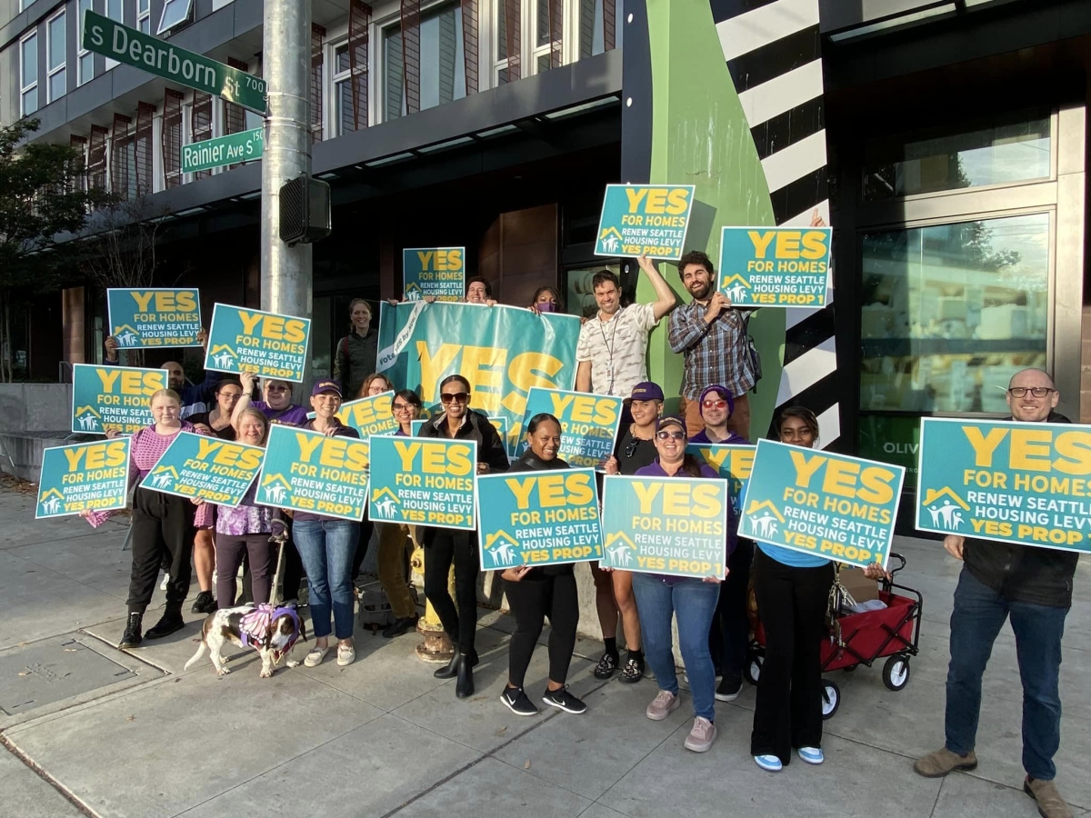 People hold signs with the message yes for homes, renew Seattle Housing Levy, yes Prop 1