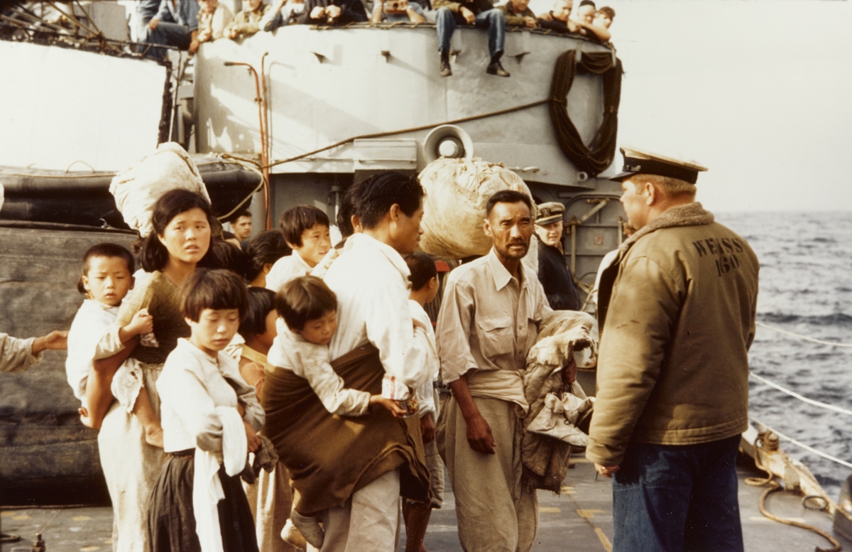 Several Korean adults and children stand in front of a ship.