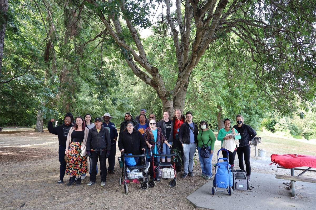 Photograph of large group of people standing under a large, leafy tree