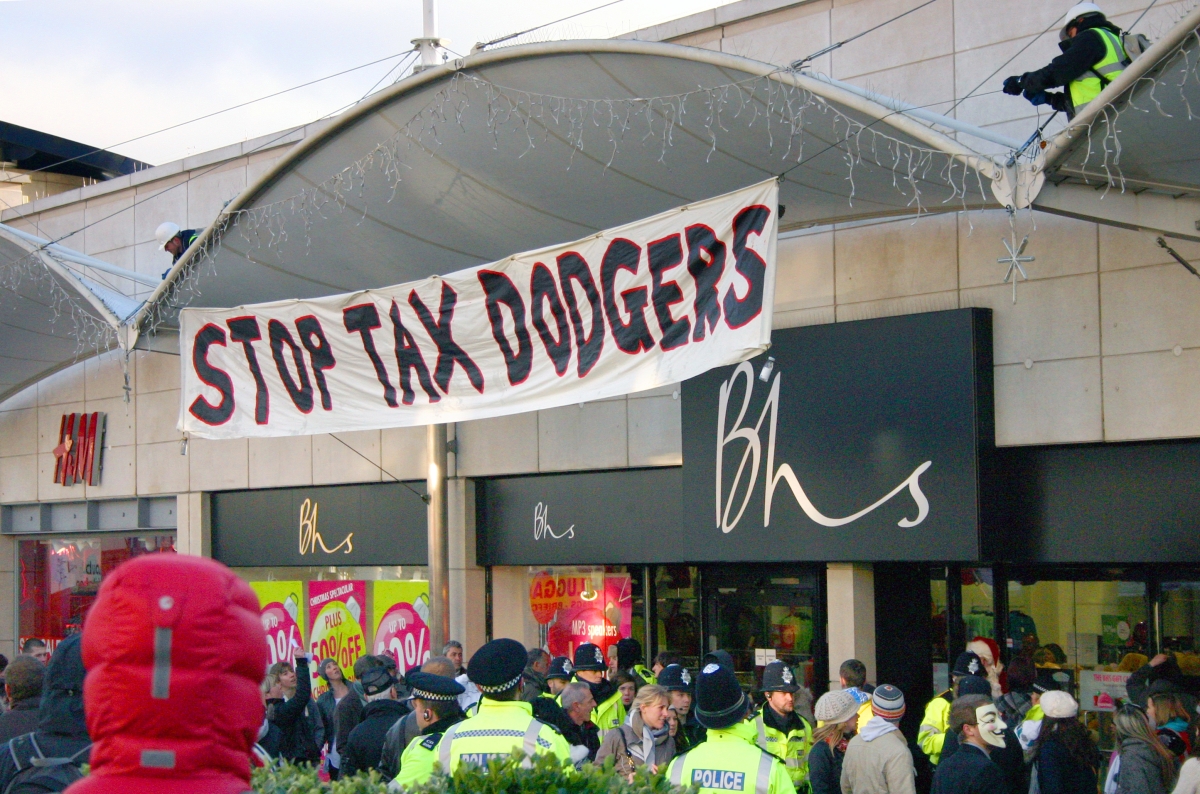 People gathered outside building under banner that reads, "Stop Tax Dodgers"