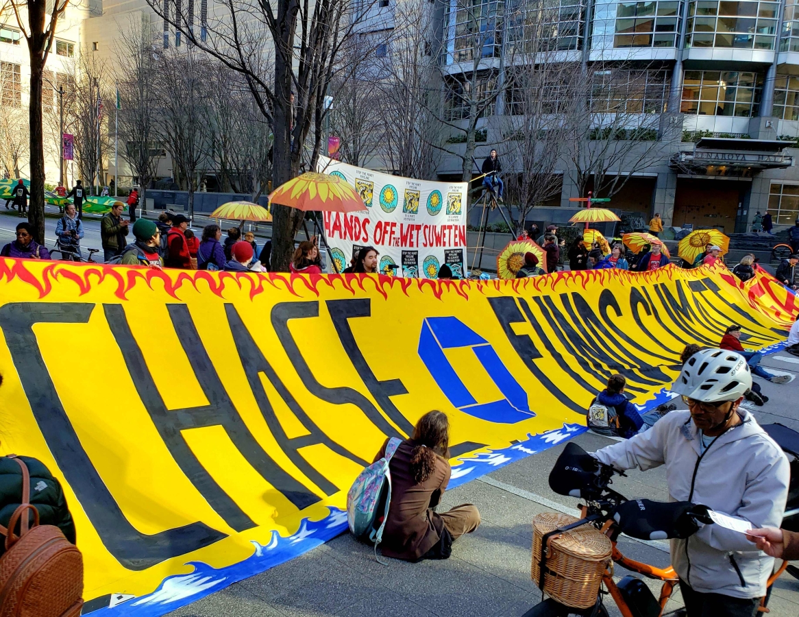 Photograph of people arrayed in front of and behind a large banner condemning Chase's relationship with the climate