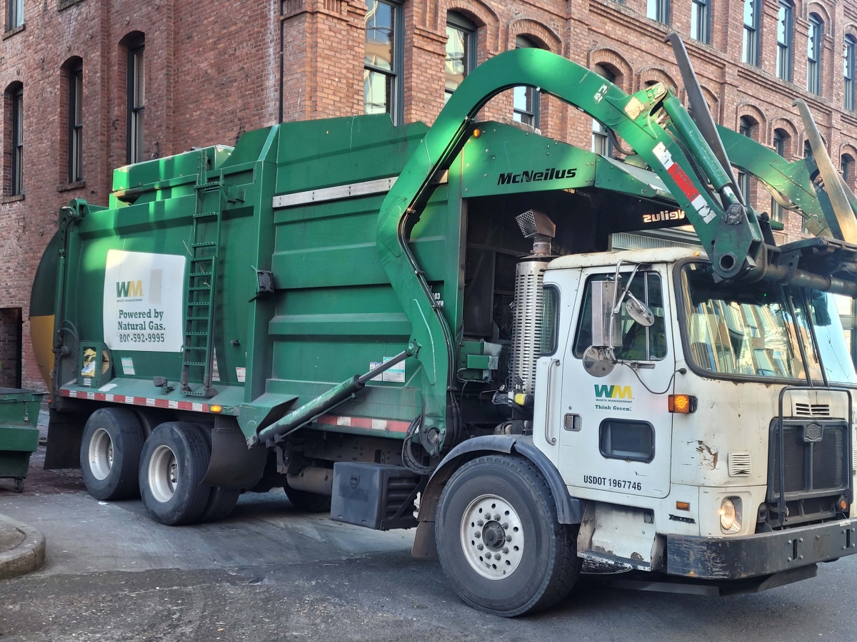 Photograph of a Waste Management truck in an alley by a brick building