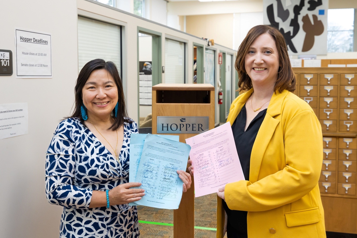 Rep. My-Lin Thai and Sen. Noel Frame stand side by side in an office, holding pieces of paper.