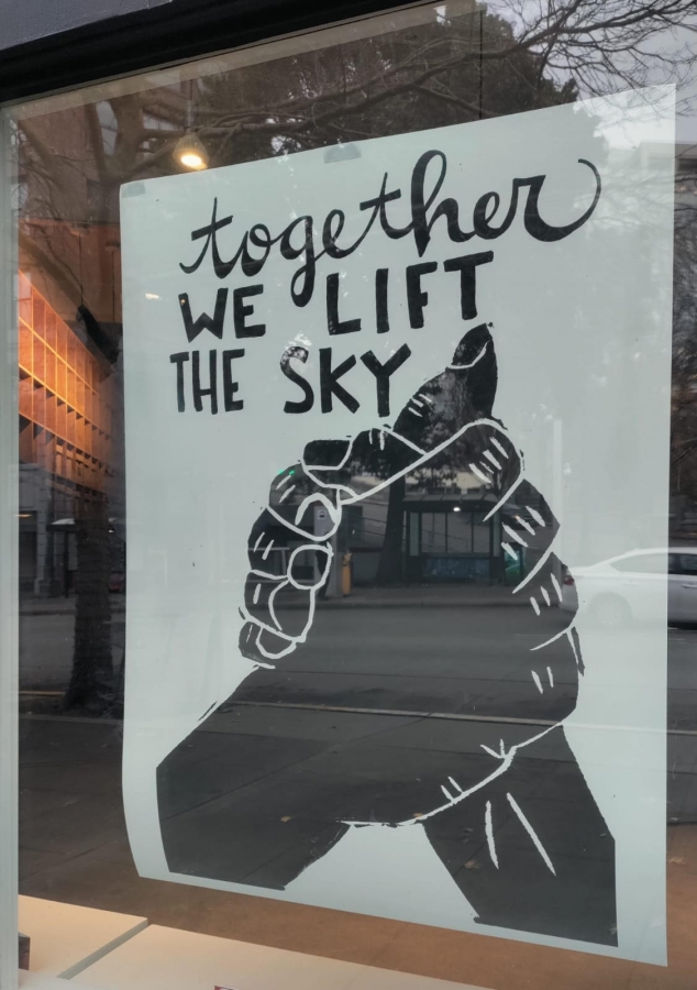 Poster in window showing two hands clasping under caption that reads, "together we lift the sky"