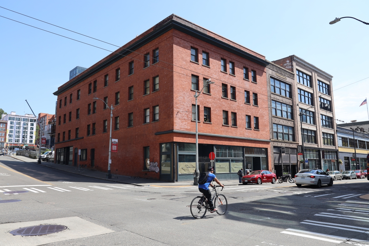 Photograph of large, square, vintage brick building on city street corner on sunny day
