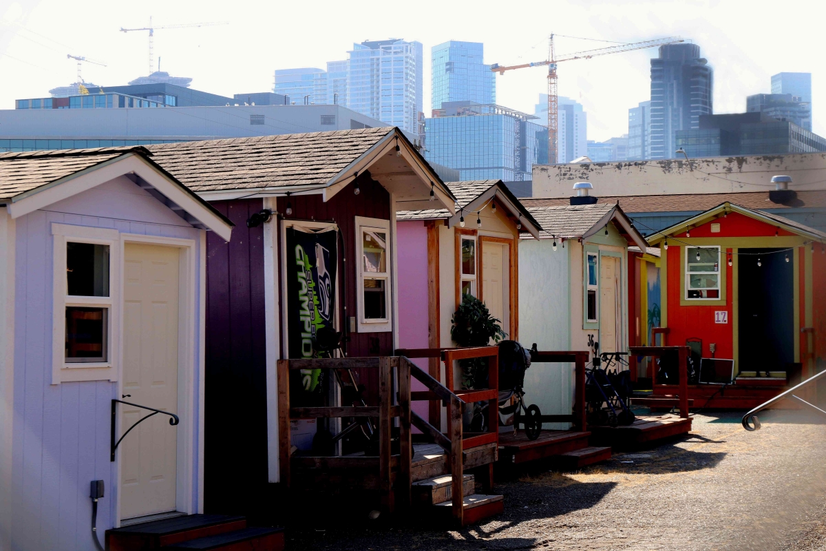 Photograph of row of tiny houses on sunny day, with city skyline visible in background
