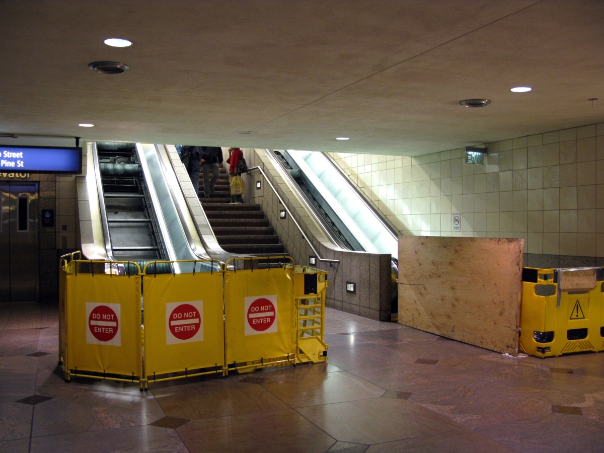 Photograph of bottom of subway escalator flight barricaded with Do Not Enter signs, next to a staircase