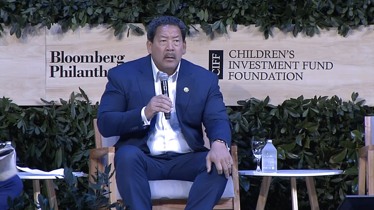 Bruce Harrell, dressed in blue suit, sits on chair holding a mic in front of a banner reading, "Bloomberg Philanthropy/ CIFF Children's Investment Fund Foundation."