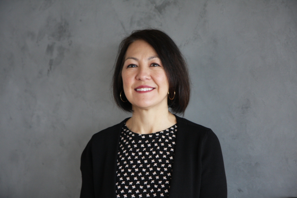 Photograph of middle-aged Asian-appearing woman with chin-length dark hair, wearing hoop earrings and black jacket over print top