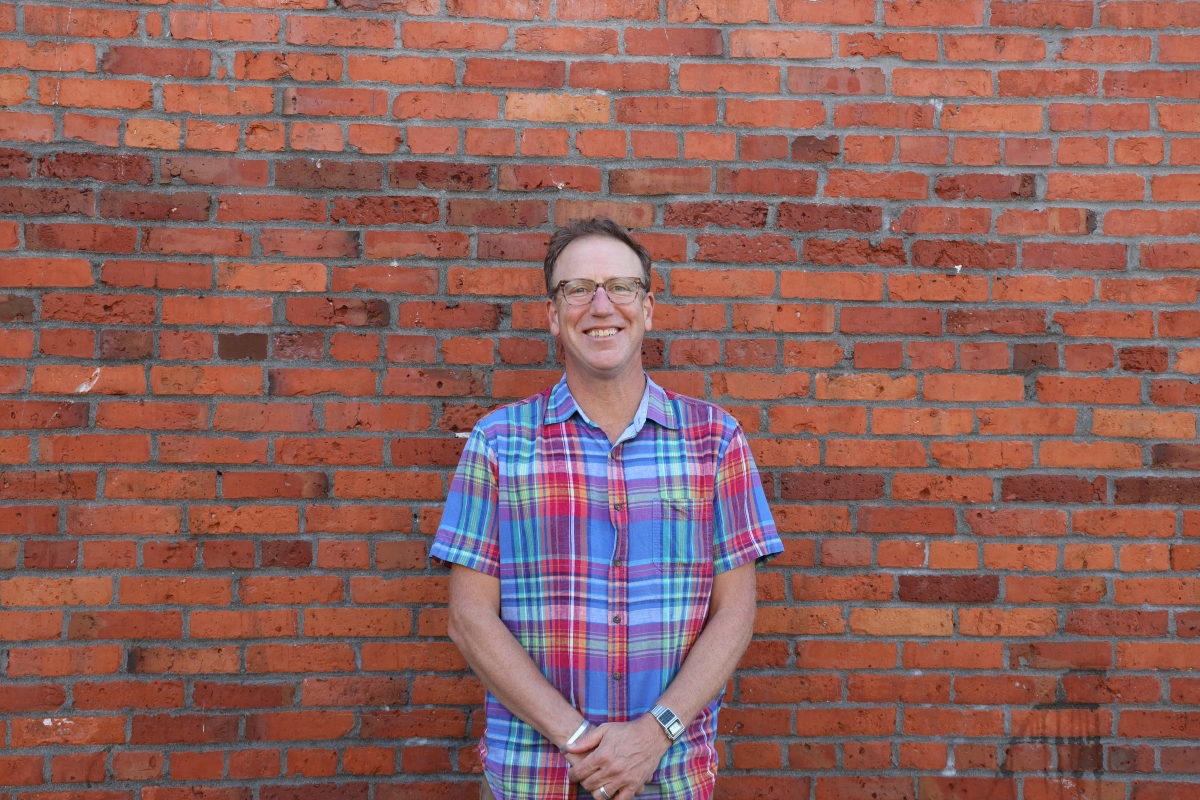 Pete Hanning, middle-aged white man wearing glasses and flannel shirt, poses against a brick wall, smiling.