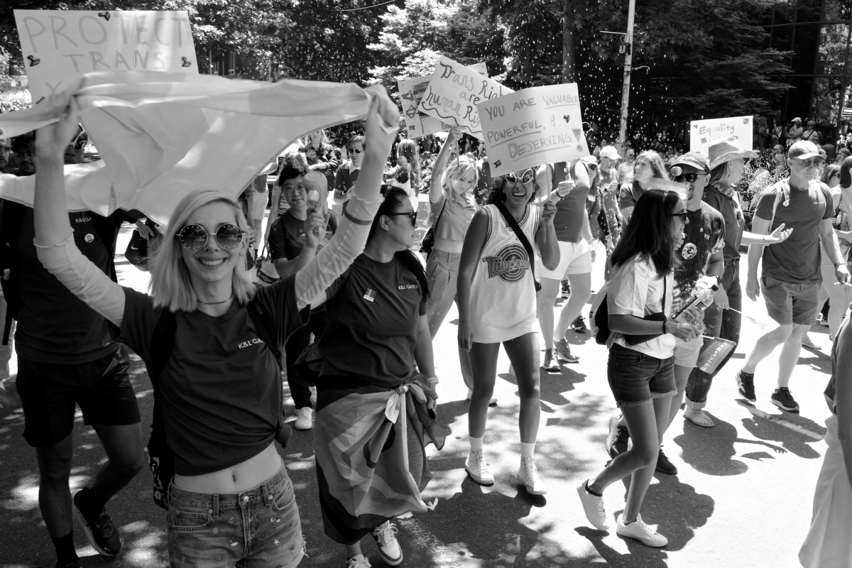 People march on a sunny street, holding up banners and signs.