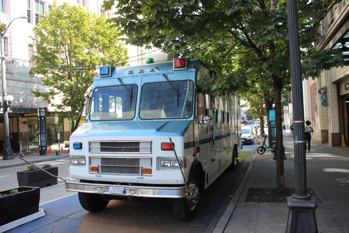 Light-blue RV parked by tree-lined sidewalk on city street