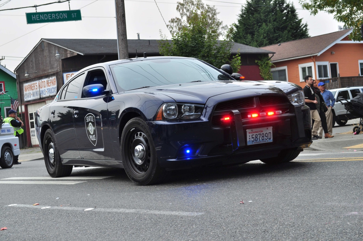 Photograph of police car parked in crosswalk, Henderson Street sign and houses and auto-repair sign visible in background