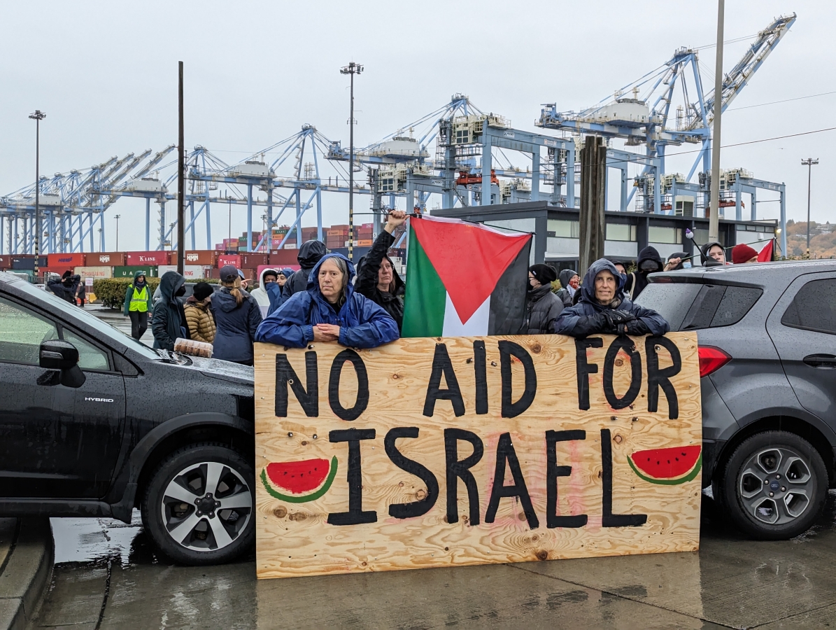 Protestors blockade road with port cranes in the background, holding a sign saying no aid for Israel