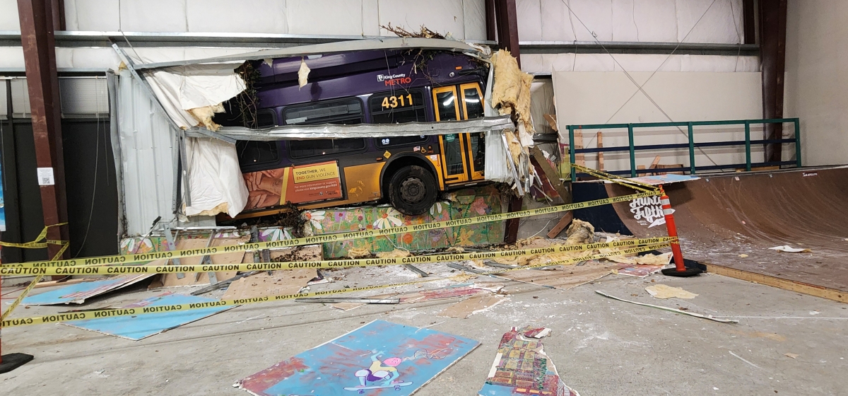A King County Metro bus is halfway through a warehouse, smashing a mural.