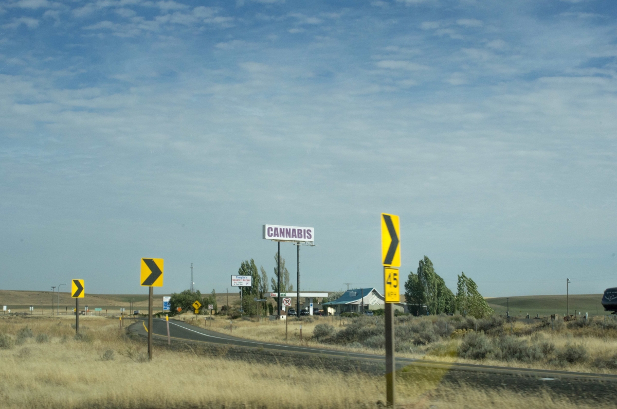 A small shopping center in a rural area with a large sign on a pole saying "cannabis"
