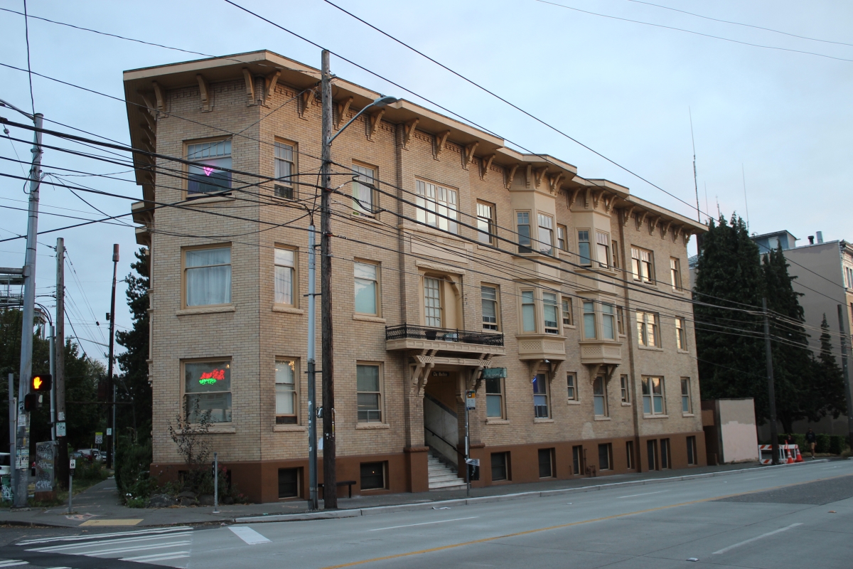 Wide-angle view of vintage, light-brown colored apartment building against dusky light-blue sky