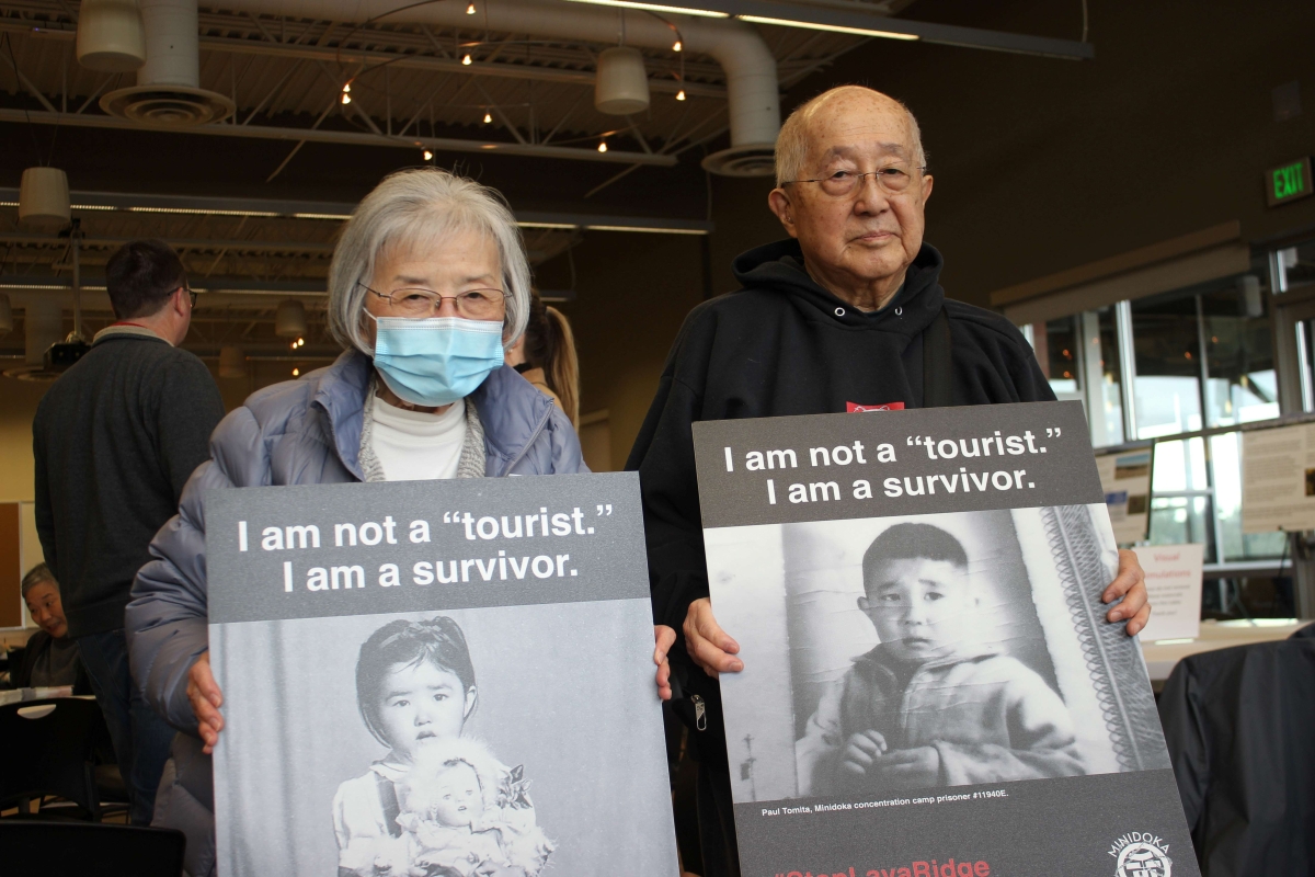 Two older Asian people, a man and a woman, each hold signs showing pictures of themselves as children, under legend, "I am not a tourist. I am a survivor."