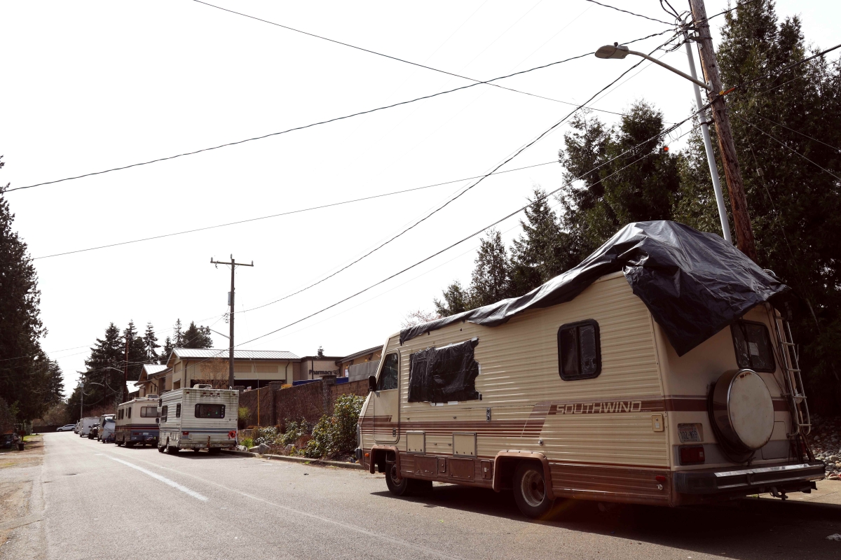 Photograph of RV, with tarp spread on top, parked by curb on residential street on a sunny day