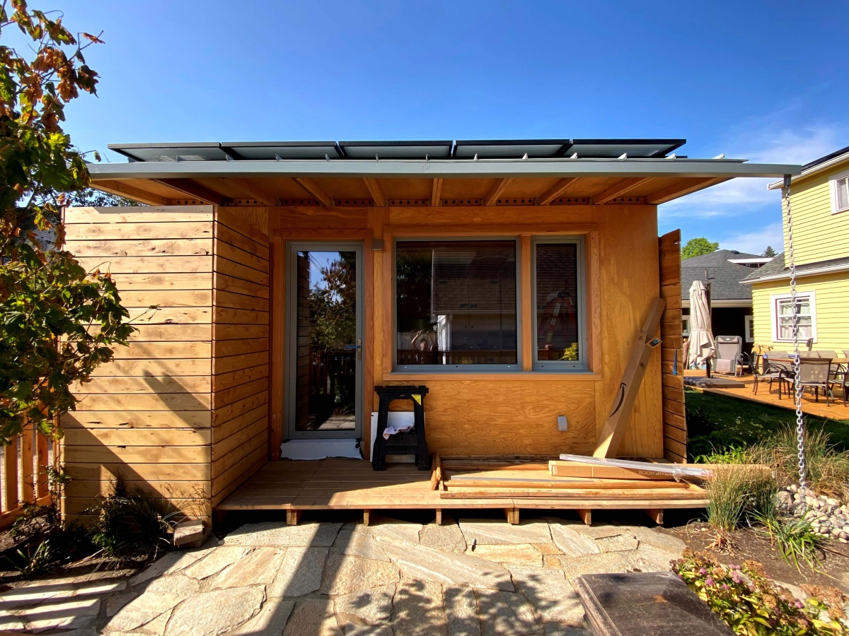 Photograph of front of bright-colored wooden house with glass-paned doors and windows, boards and trestle set on front deck