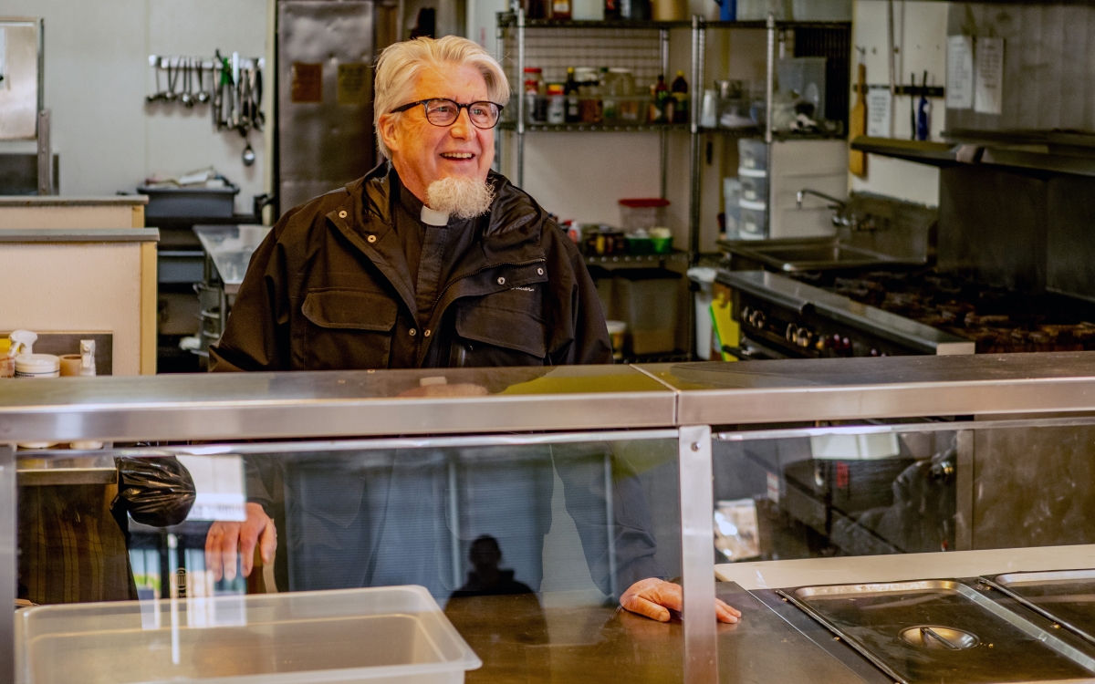 Rick Reynolds, older white man with goatee and dressed in barn jacket, stands behind cafeteria-style counter.