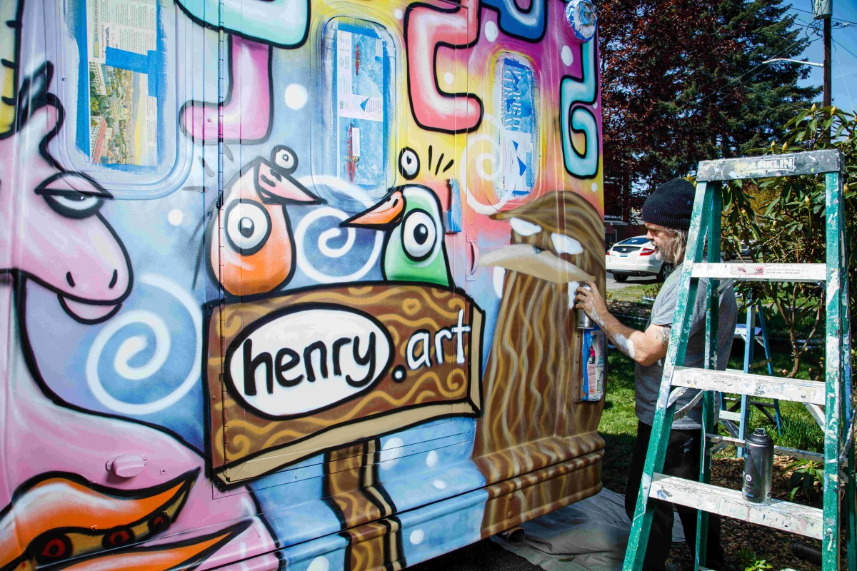 Man in knit cap works at corner of large mural with a spray can.