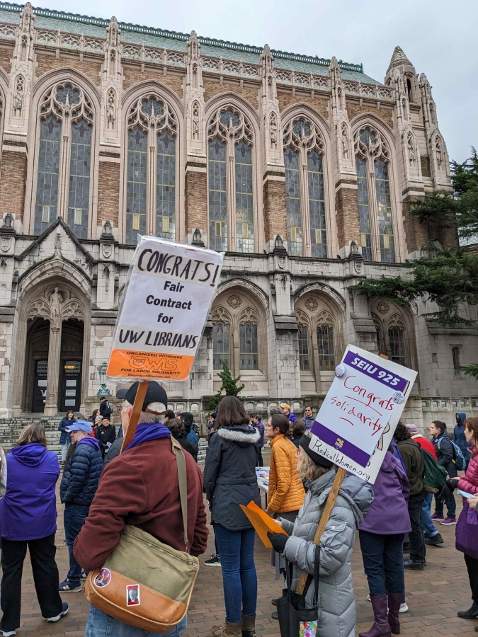 People holding signs supporting librarians' solidarity stand outside Gothic-style Suzzallo Library on the UW campus.