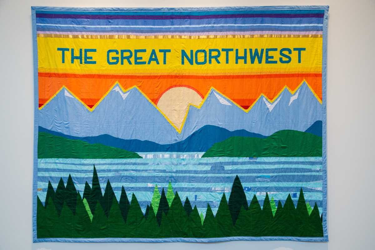 A Joey Veltkamp quilt with mountains and a sunset, that reads "The Great Northwest"