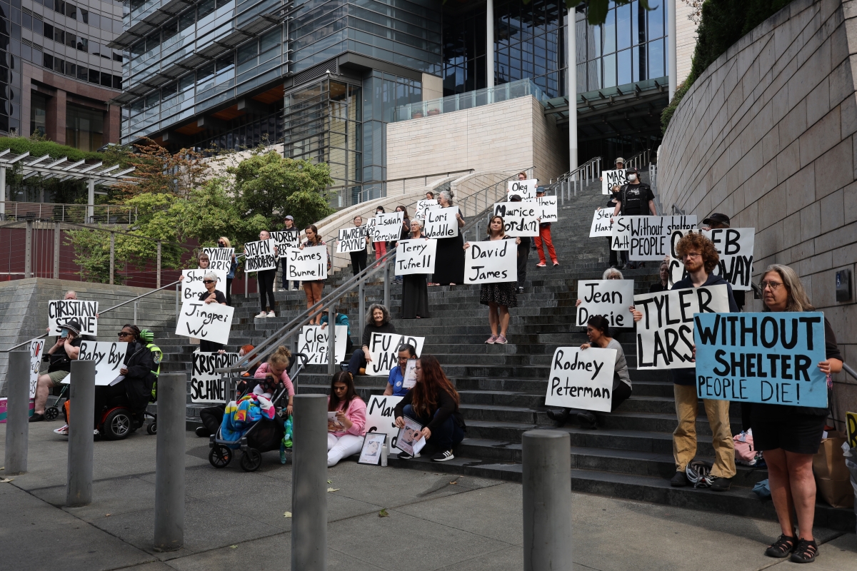 People stand on courthouse steps holding large placards with names.