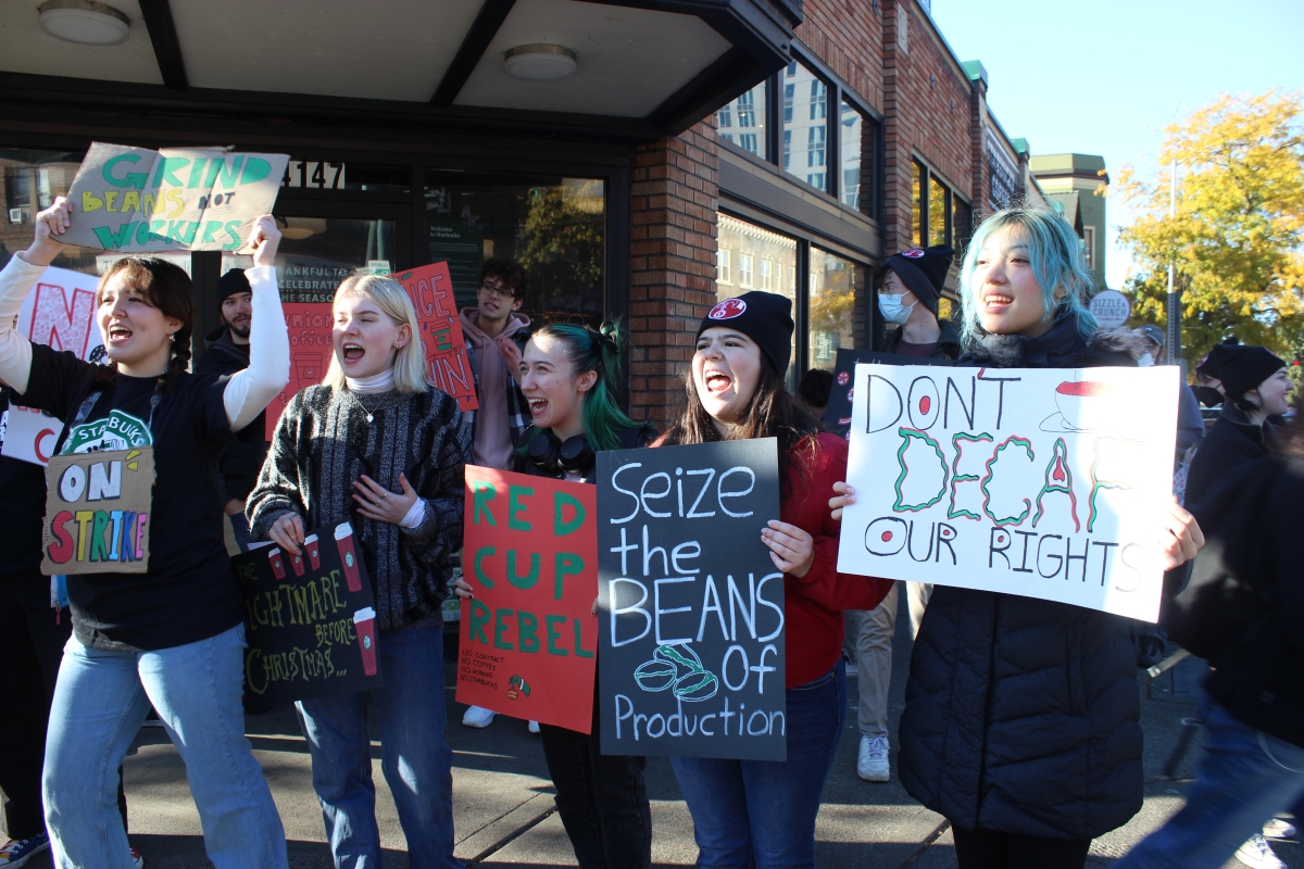 Several young women hold colorful picket signs on a street corner outside a Starbucks shop.