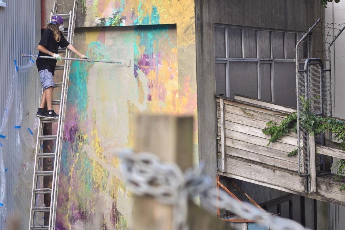 An artist from New Zealand, who will exhibit in the show, works on removing graffiti from a building. 