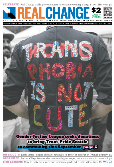 Person seen from the back wearing a black shirt with letters reading, "Transphobia Is Not Cute" in glittery letters