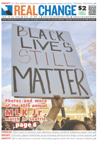 Photograph of brown-skinned woman's hand holding sign reading, "Black Lives Still Matter," backed by crowd of faces on city street