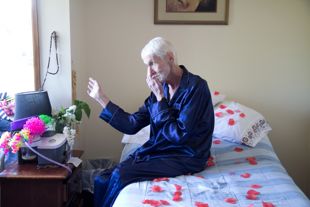 Robert Baxter-Fuller sits on his bed in blue pajamas. The clock, above, ticked down the minutes until 3 p.m. when Fuller would ingest his life-ending medications. Photo by Wes Sauer