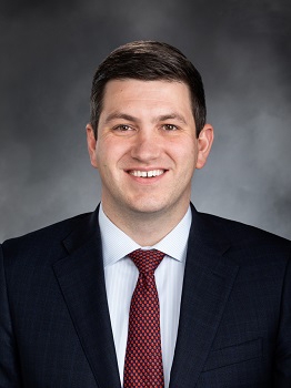 Smiling young white man with short dark hair, in suit and tie