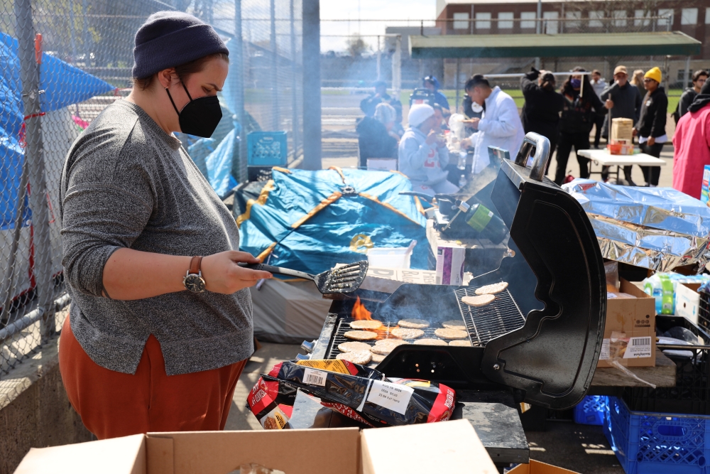 A community member grills hamburgers for lunch for the asylum-seekers camped at the tennis court, April 3.