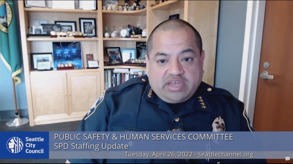 Screenshot of Adrian Diaz speaking in front of bookcase at online Public Safety meeting
